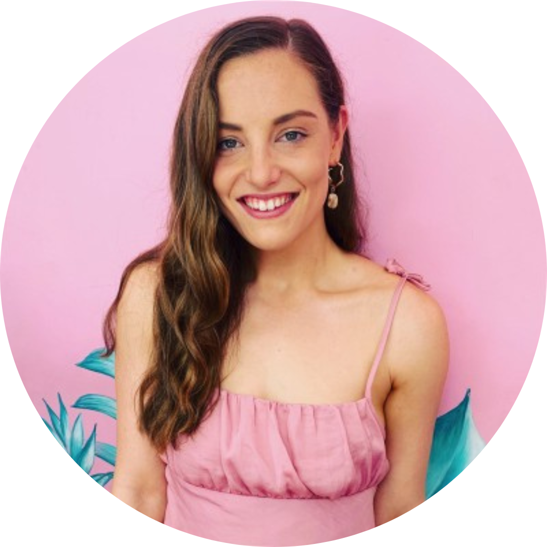 Caitlin DeMarco, a woman with long brown hair, fair skin, wearing a pink singlet against a pink wall.
