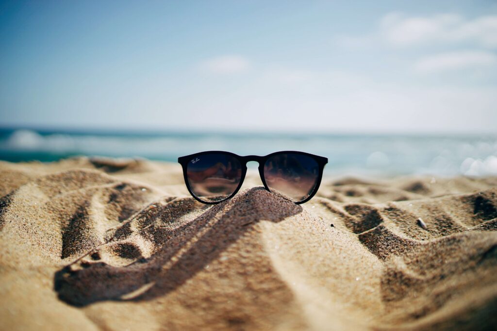 Black sunglasses on the sand with the ocean in the background